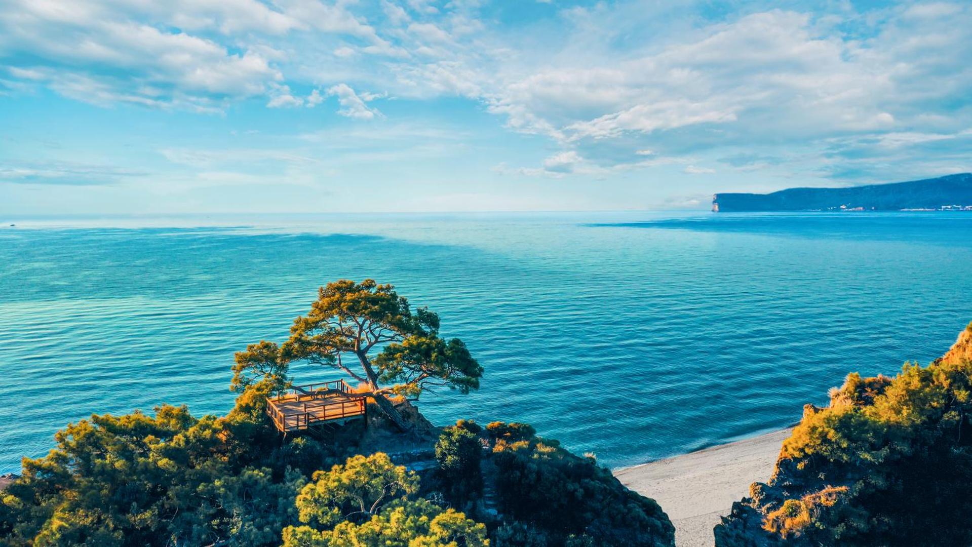 NG Phaselis Bay koka skatu platforma uz klints piekrastē ar vientuļu priedi un skatu uz dzidro Vidusjūru saulainā dienā