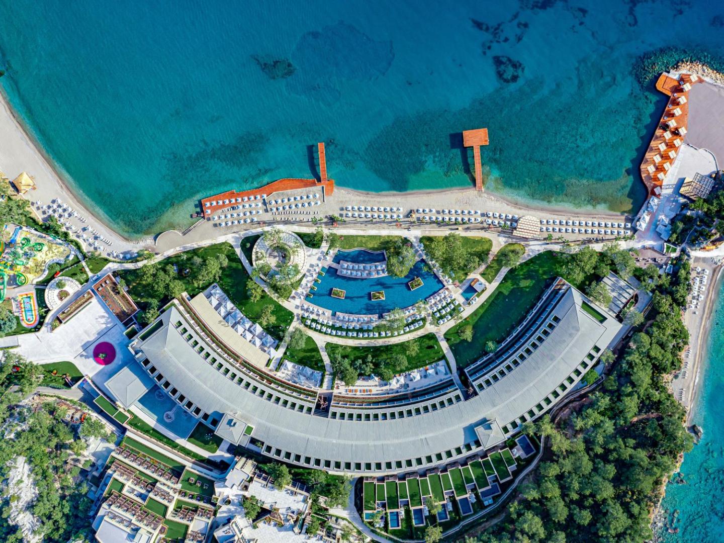 NG Phaselis Bay viesnīcas teritorijas skats no putna lidojuma Kemerā — privātā pludmale, piestātnes, baseini un priežu meža ieskauta arhitektūra