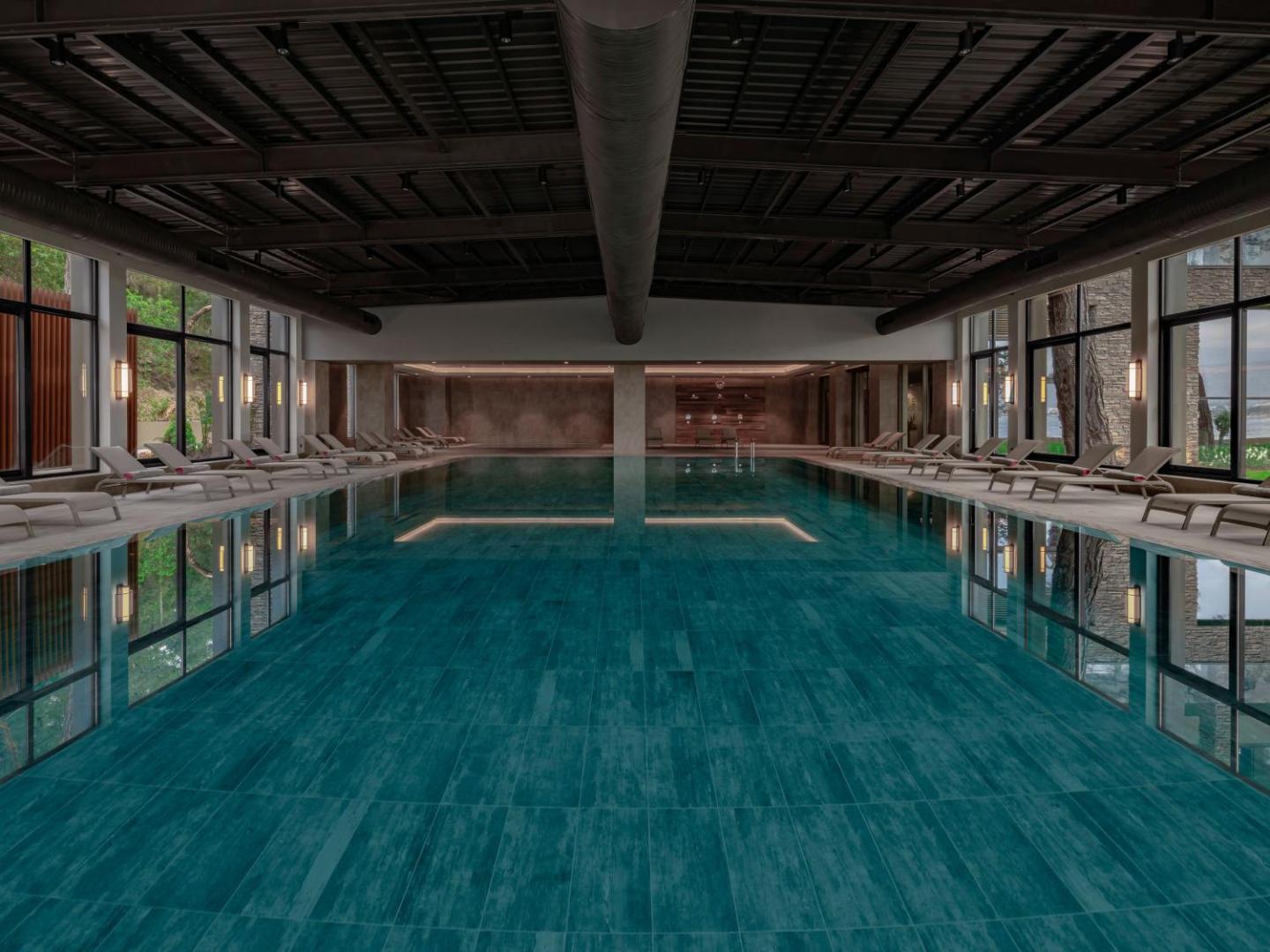 NG Phaselis Bay moderns iekštelpu baseins ar panorāmas logiem un atpūtas krēsliem — mierīga gaisotne spa zonā