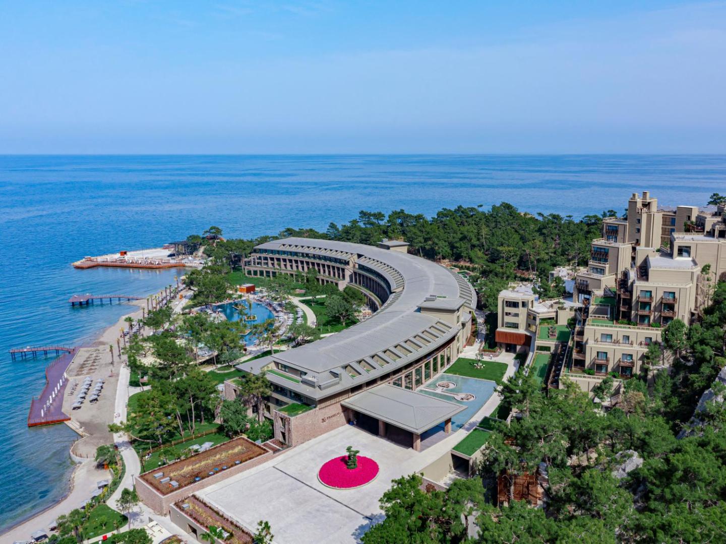 NG Phaselis Bay modernā arhitektūra un ieeja — skats uz viesnīcas korpusiem, zaļo zonu un jūras horizontu Kemeras piekrastē