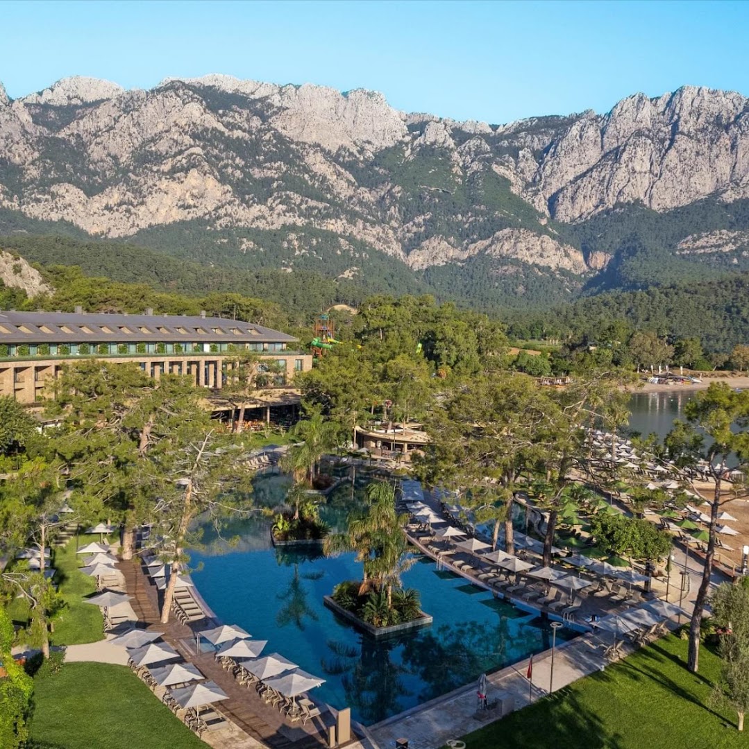 NG Phaselis Bay āra baseins ar palmām un sauļošanās krēsliem uz iespaidīgu kalnu grēdas fonu Kemeras reģionā, Turcijā