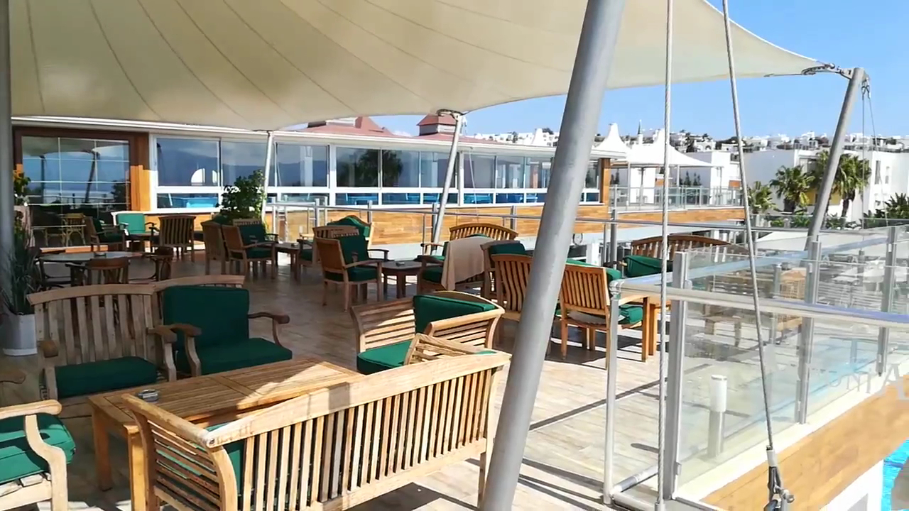 Armonia Holiday Village & Spa atpūtas zona uz terases zem lielas saules nojumes ar koka mēbelēm un stikla margām