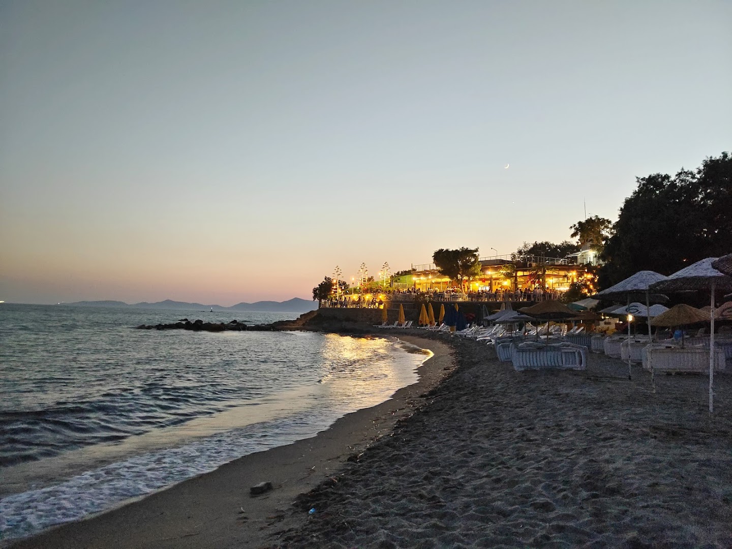 Armonia Holiday Village & Spa piekrastes restorāns vakarā ar izgaismotu terasi un galdiņiem pie pašas Egejas jūras