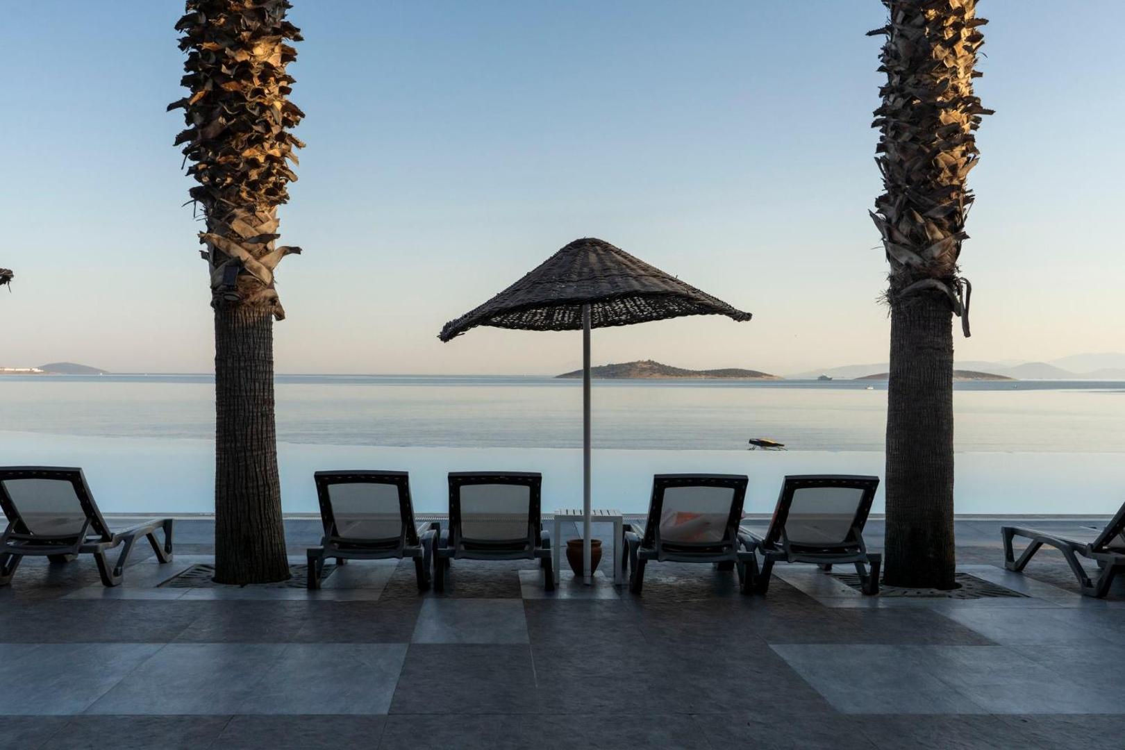 Atpūtas zona Blue Dreams Resort & Spa ar sauļošanās krēsliem un salmu saulessargu starp divām palmām, skats uz mierīgu jūru.