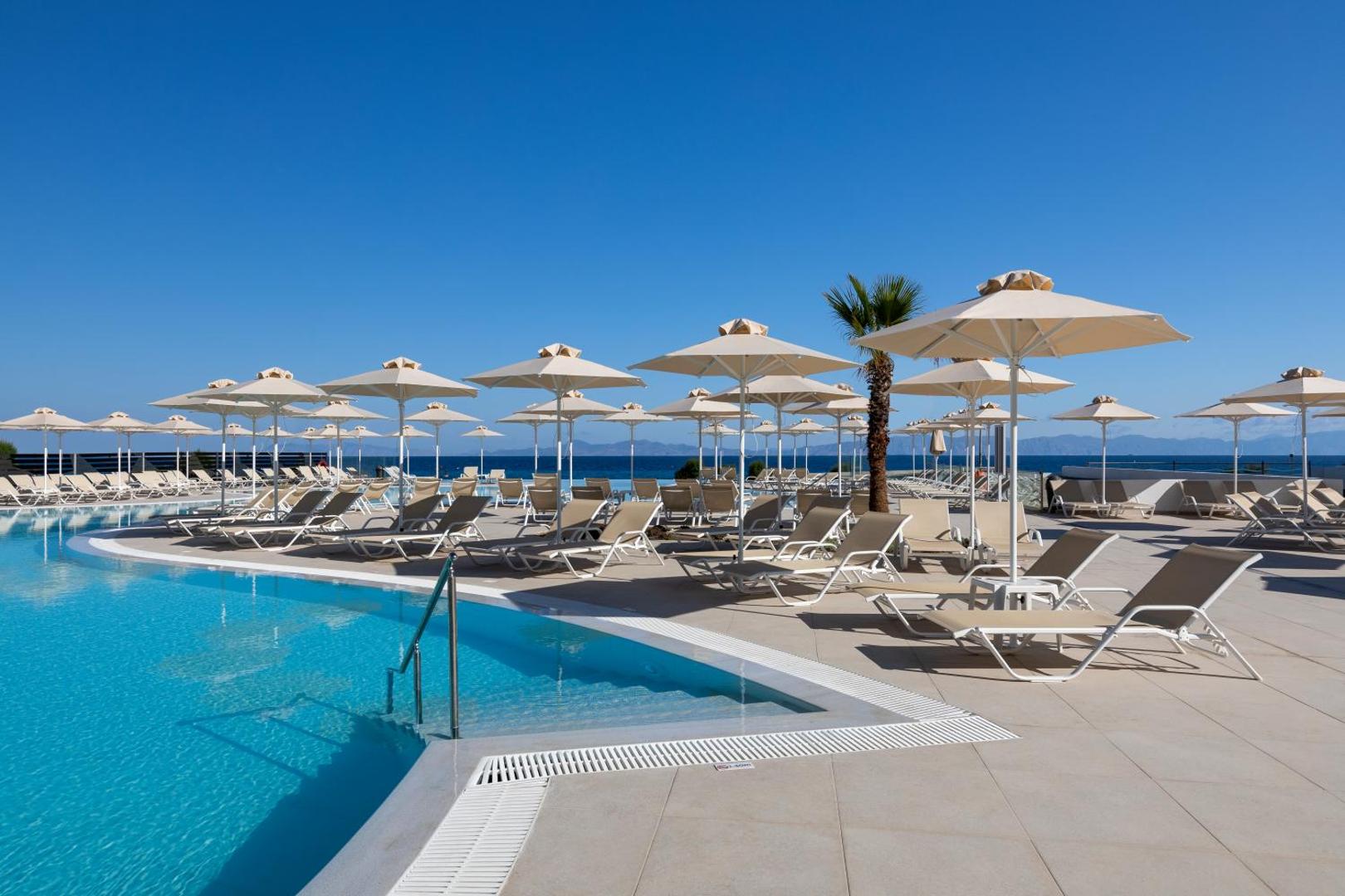 Atpūtas zona pie Belair Beach baseina ar gaišiem saulessargiem un ērtiem zviļņiem zem skaidrām debesīm Rodā