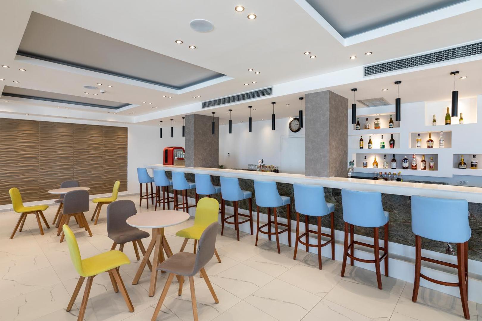 Belair Beach viesnīcas lobby bārs Rodas salā ar modernu interjeru, gaiši zilām bāra koka krēsliem un plašu dzērienu izvēli.