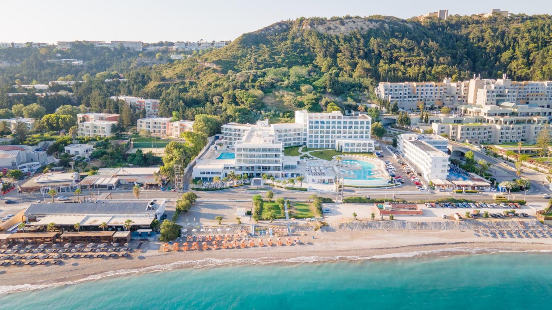 Belair Beach viesnīcas panorāmas skats no putna lidojuma Rodas salā — balta ēka pie Egejas jūras krasta ar baseiniem un pludmali