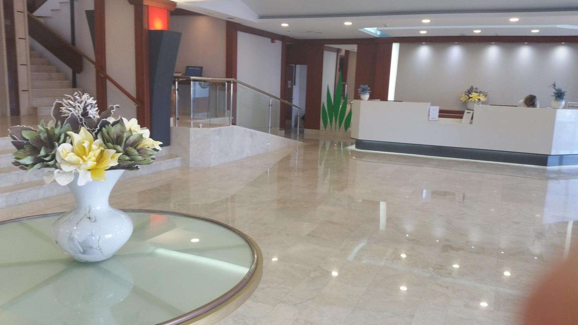 Belair Beach viesnīcas vestibila interjera detaļa ar ziedu kompozīciju un skatu uz recepcijas galdiem Rodas salā