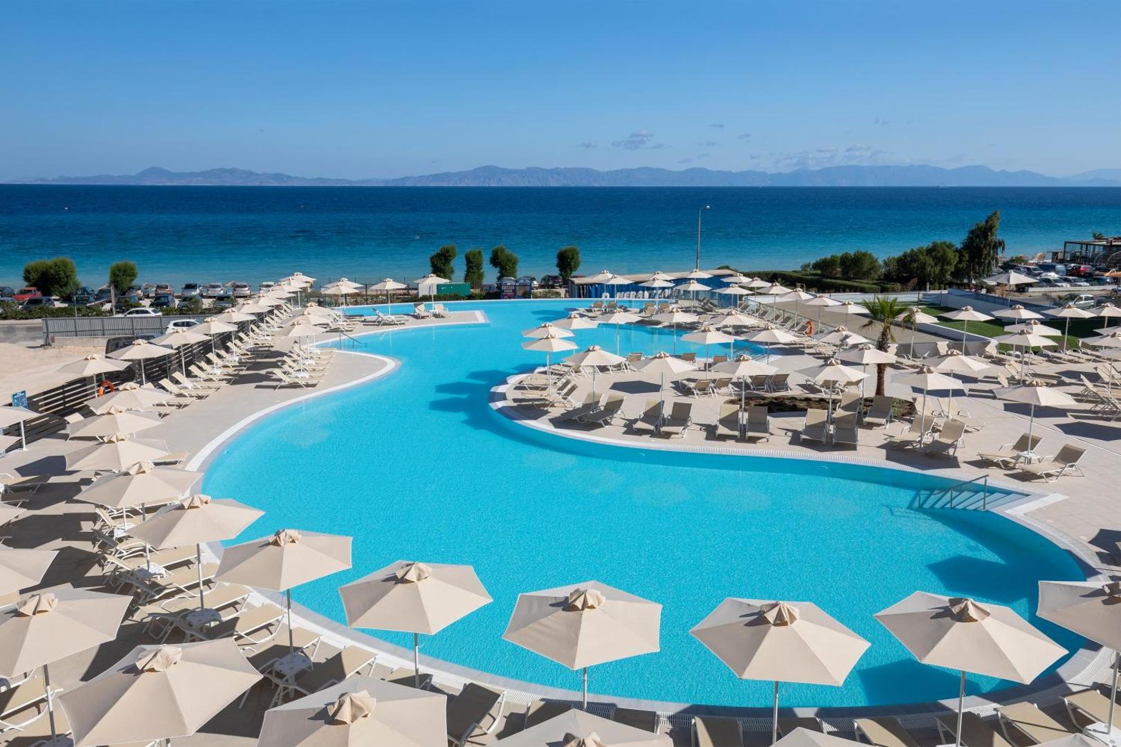Belair Beach viesnīcas lielais āra baseins Rodas salā ar skatu uz jūru, saulessargiem un atpūtas krēsliem saulainā dienā