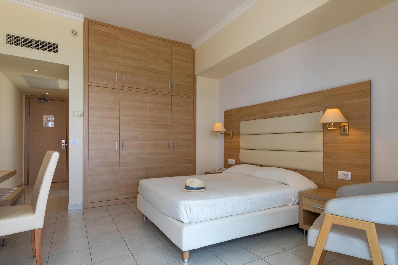 Gaišs Belair Beach viesnīcas numurs ar koka mēbelēm un iebūvēto skapi — elegants interjers atpūtai Rodas piekrastē