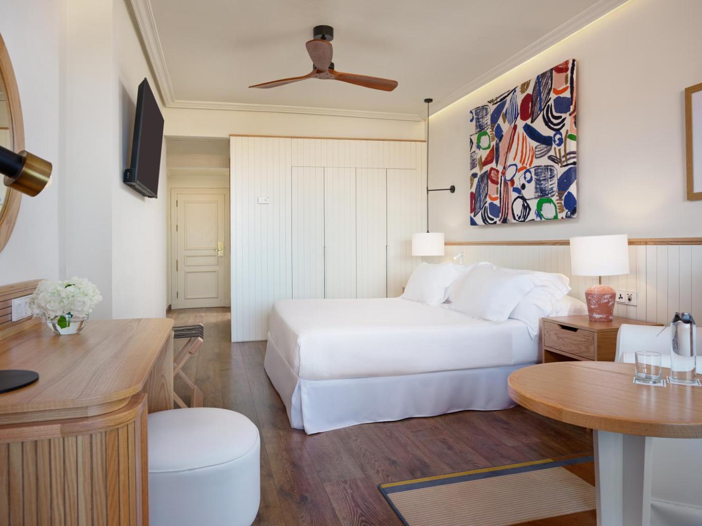 H10 Costa Adeje Palace moderns numurs Tenerifē ar gaišu interjeru, koka grīdu, mākslas darbu pie sienas un griestu ventilatoru