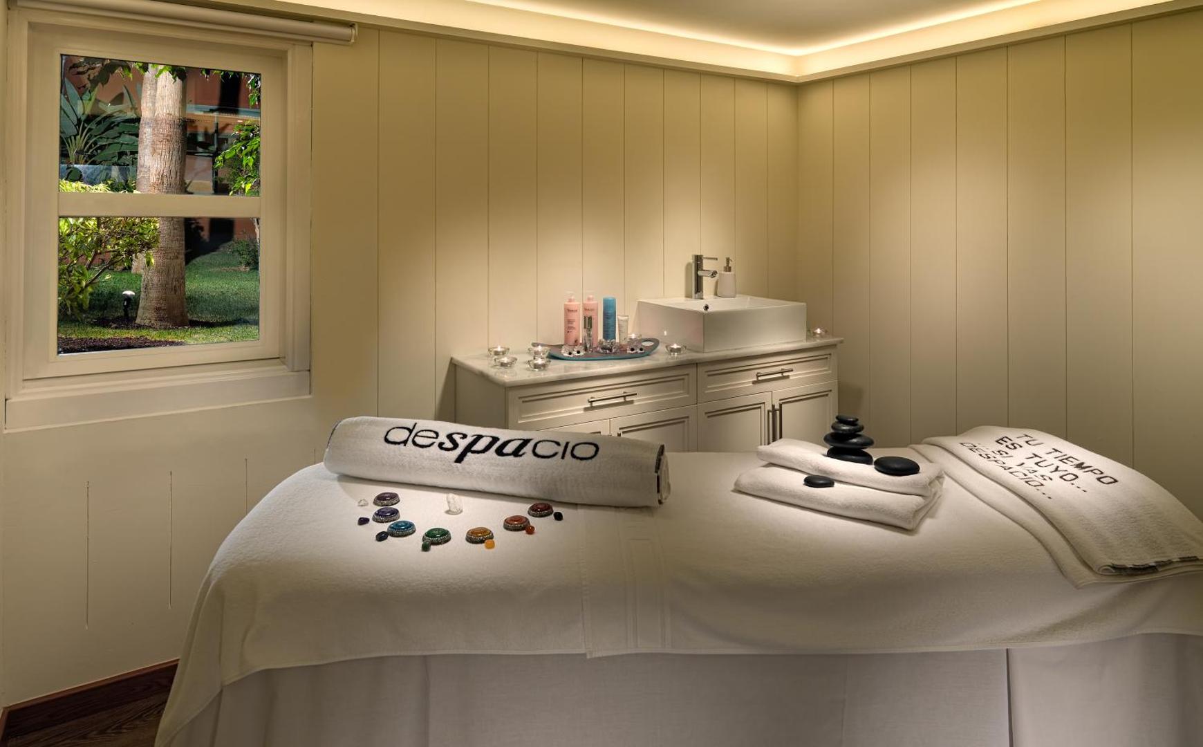 H10 Costa Adeje Palace Despacio spa procedūru numurs ar masāžas galdu, akmeņiem un mierīgu apgaismojumu relaksācijai