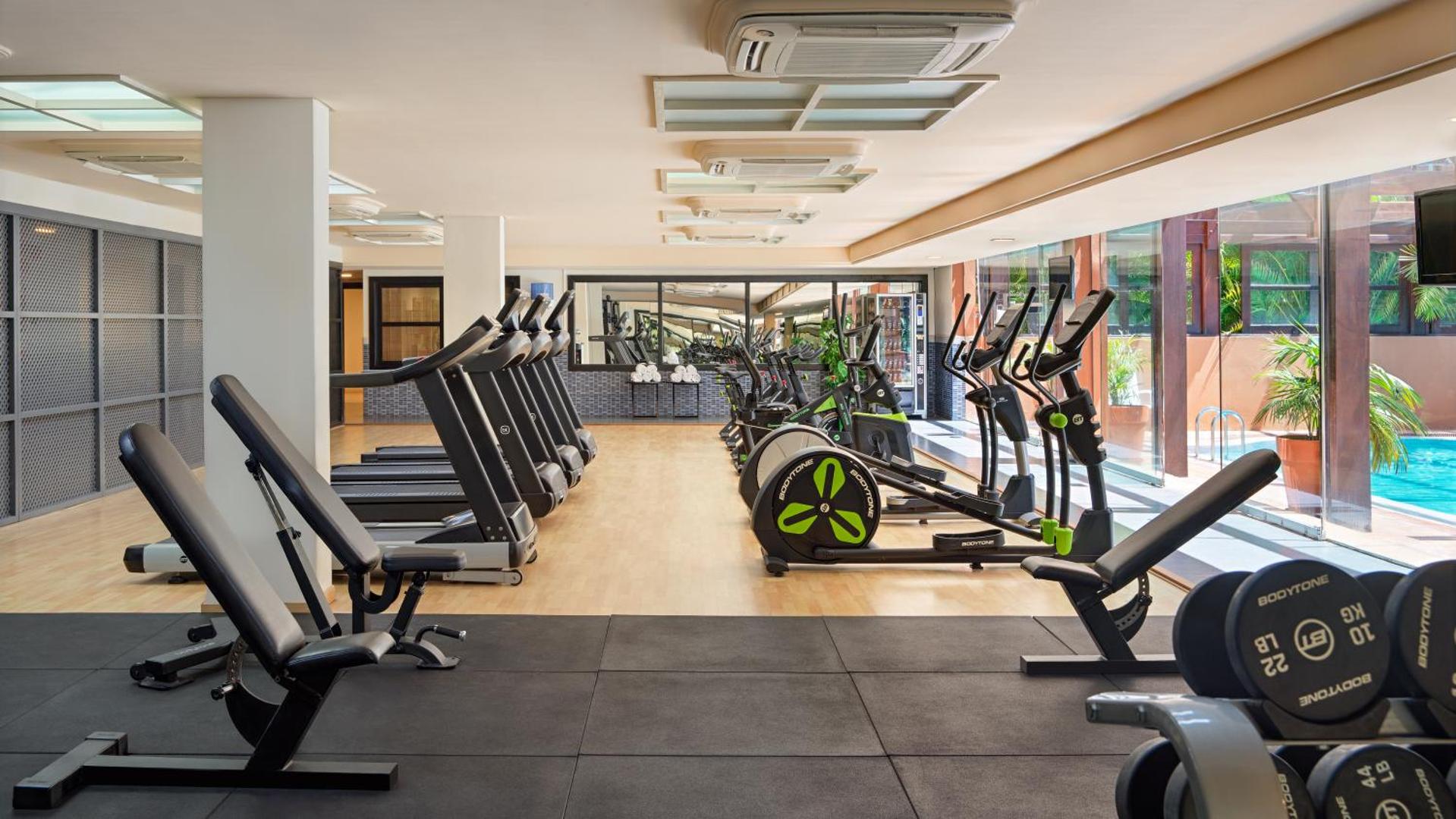 H10 Costa Adeje Palace viesnīcas fitness centrs ar moderniem skrejceliņiem un trenažieriem — gaiša telpa ar skatu uz āra baseinu