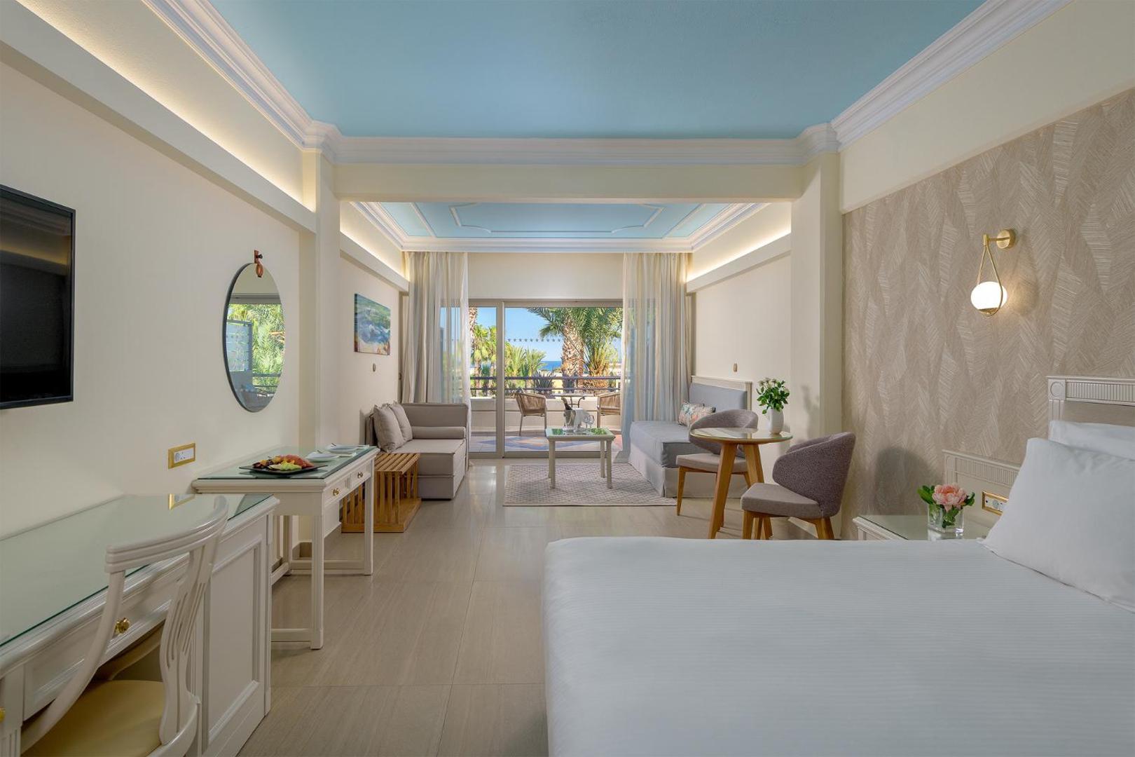 Atrium Palace viesnīcas numurs ar gaišu interjeru, atpūtas zonu un balkonu, no kura paveras skats uz dārzu