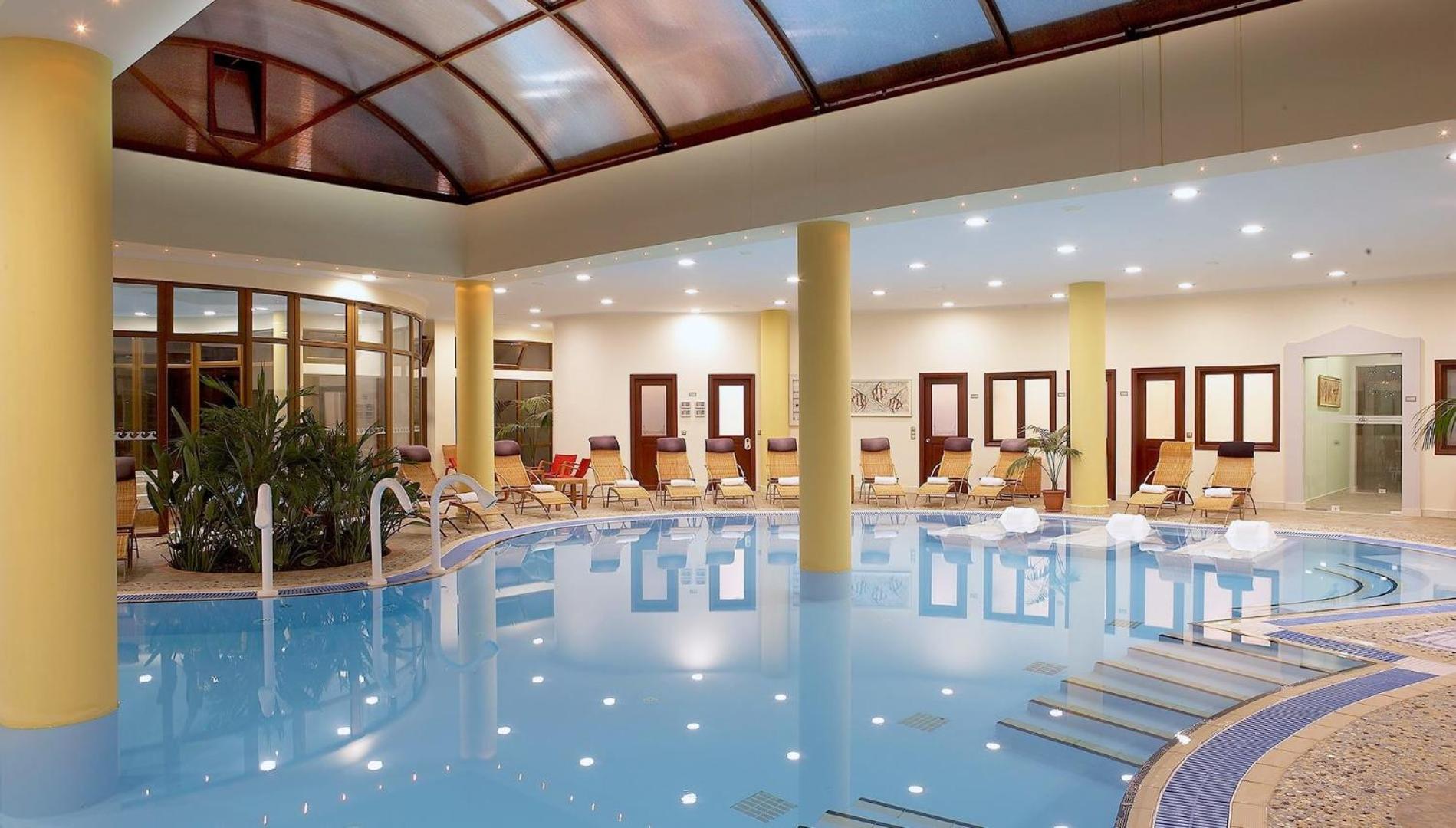 Atrium Palace viesnīcas iekštelpu spa baseins ar stikla jumtu un atpūtas krēsliem — plaša relaksācijas zona Rodas kūrortā