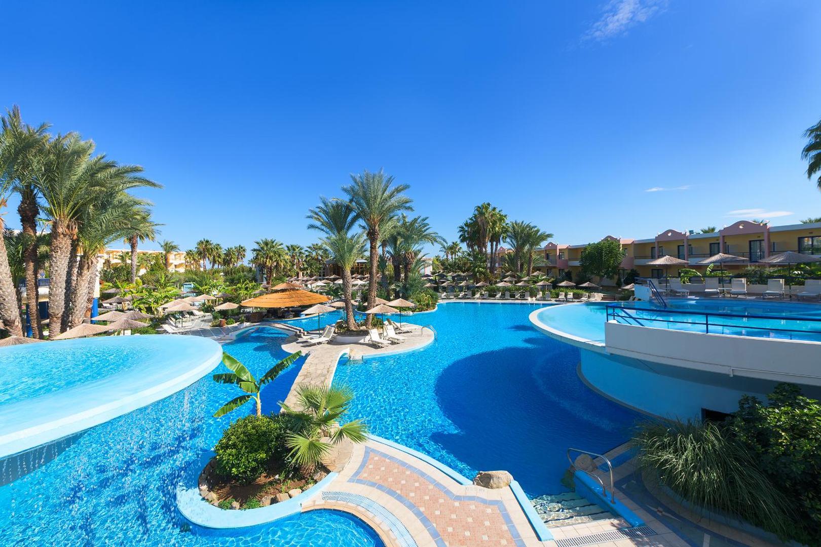 Atrium Palace Thalasso Spa Resort plašā teritorija ar vairākiem ziliem baseiniem, palmām un saulessargiem Rodas salā, Grieķijā.