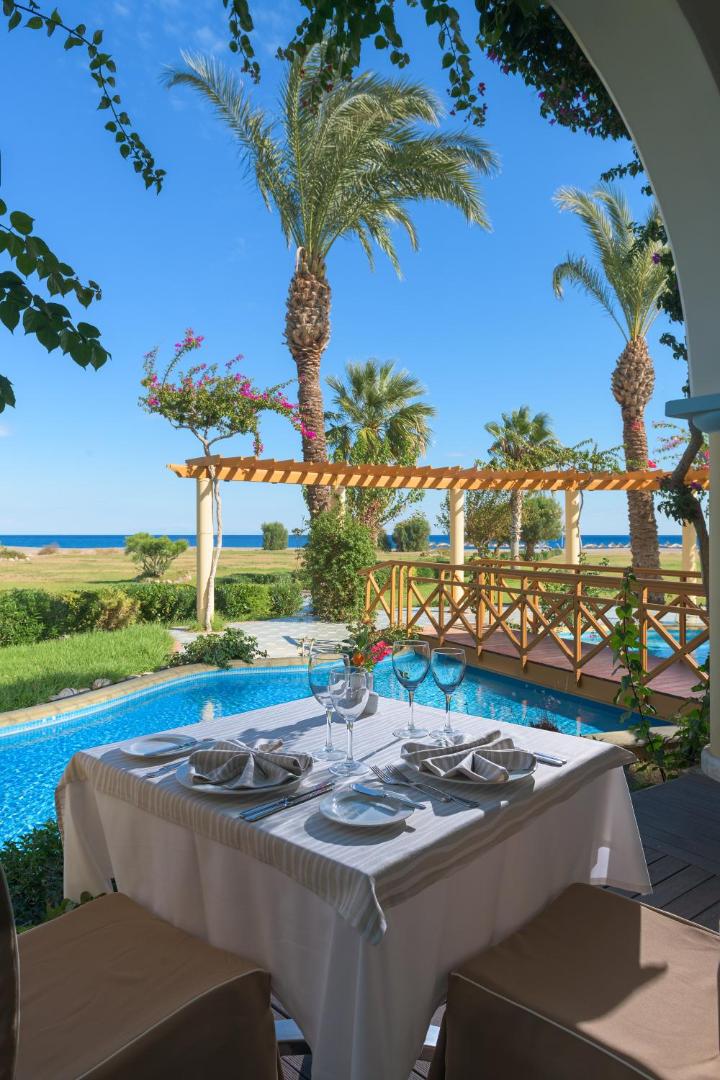 Atrium Palace Thalasso Spa Resort And Villas restorāna galdiņš ar skatu uz jūru un palmām Rodas salā pie baseina