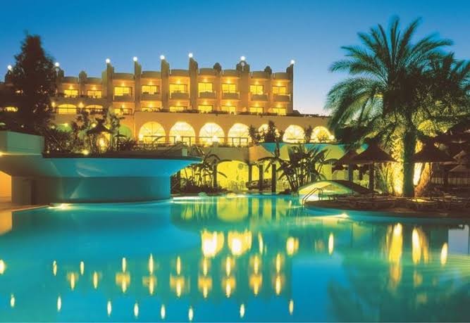 Atrium Palace Thalasso Spa Resort galvenā ēka vakarā ar izgaismotu baseinu un palmām Rodas piekrastē