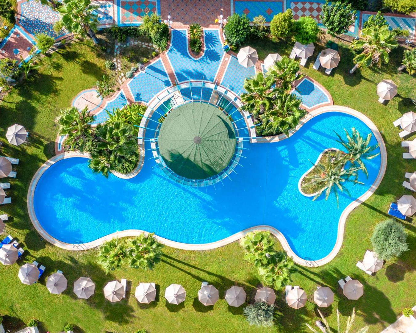 Atrium Palace Thalasso Spa Resort And Villas skats no augšas uz zilo āra baseinu Rodas salā, ko ieskauj zaļš zāliens un palmas