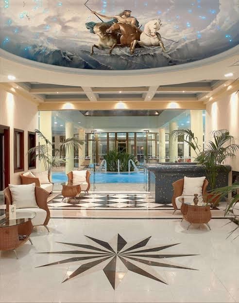 Atrium Palace Thalasso Spa Resort iekštelpu baseina zona ar dekoratīvu griestu gleznojumu, atpūtas krēsliem un skatu uz āra baseinu