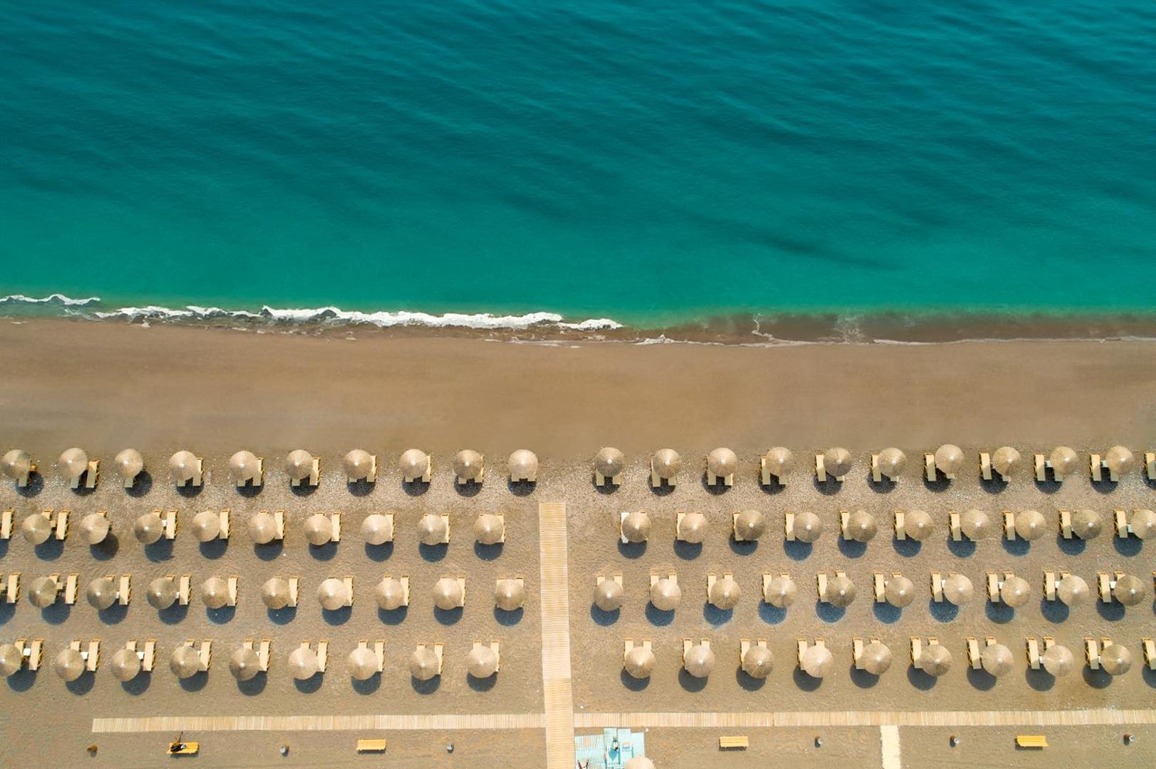 Atrium Palace Thalasso Spa Resort privātā pludmale Rodā no putna lidojuma — tirkīza jūra un sakoptas saulessargu rindas smiltīs