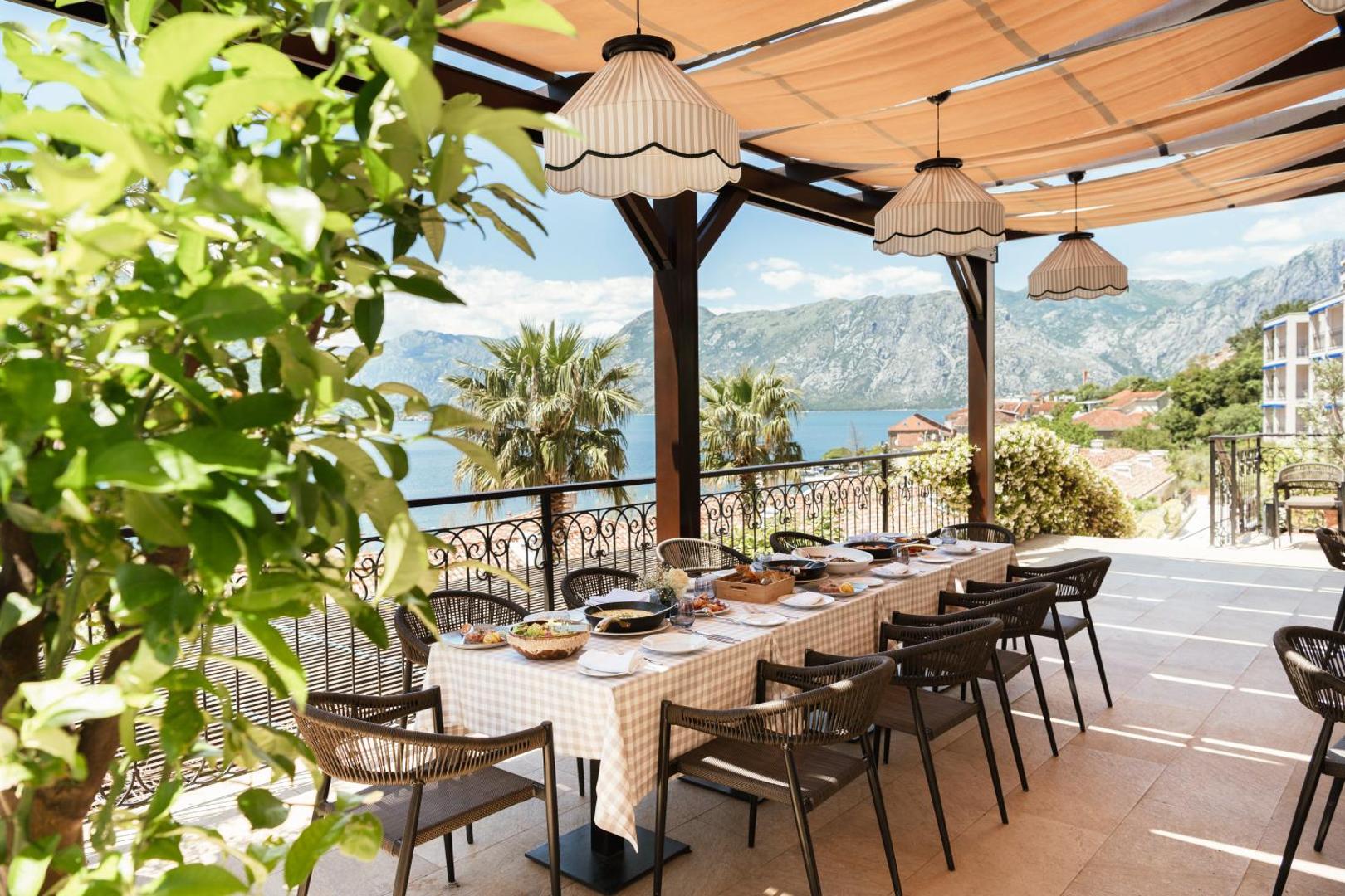 HUMA Kotor Bay Hotel & Villas āra terase ar klātu galdu, saulessargiem un panorāmas skatu uz līci