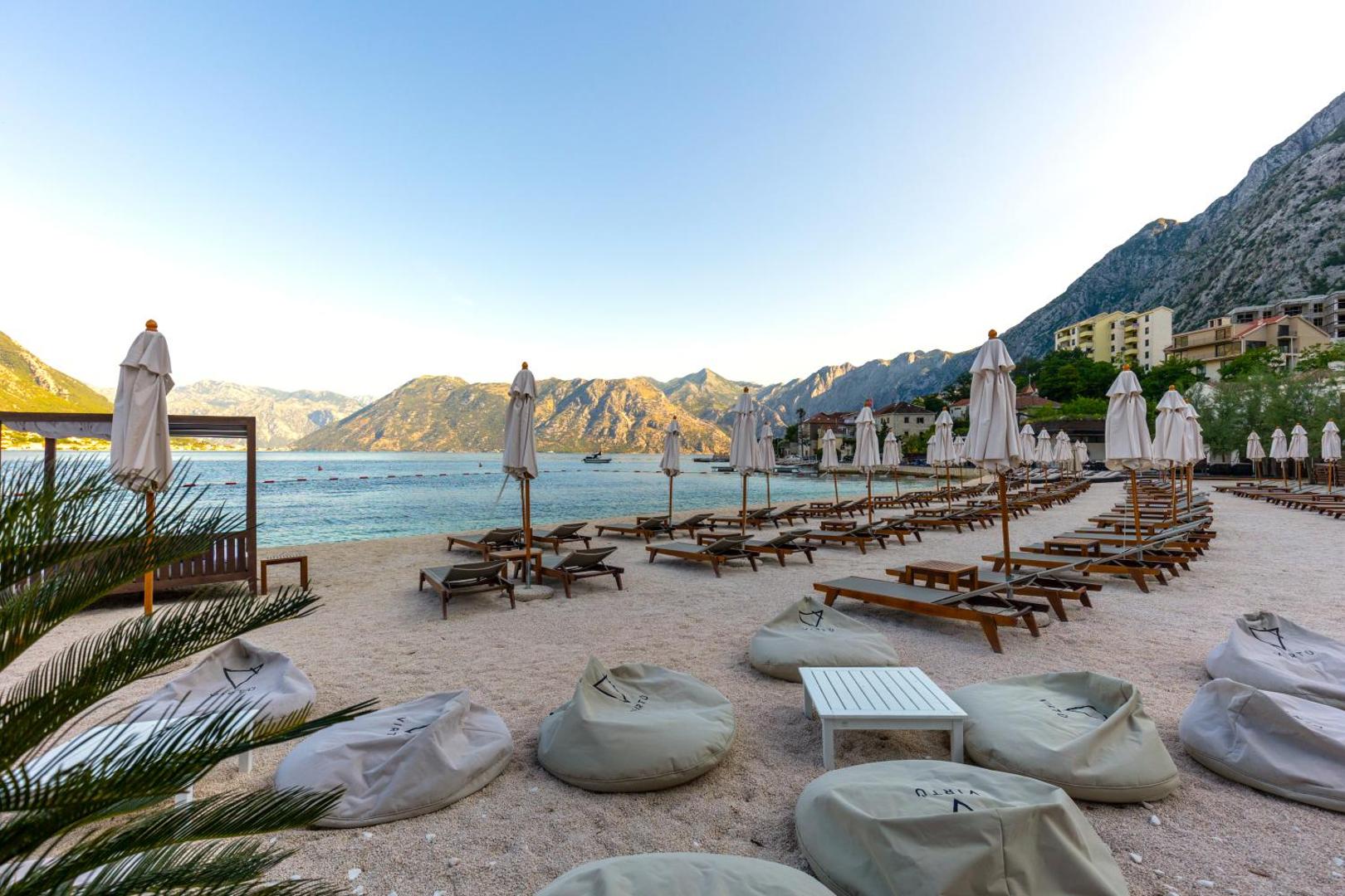 HUMA Kotor Bay Hotel & Villas privātā pludmale ar gaišām smiltīm, sauļošanās krēsliem un sēžammaisiem pie līča