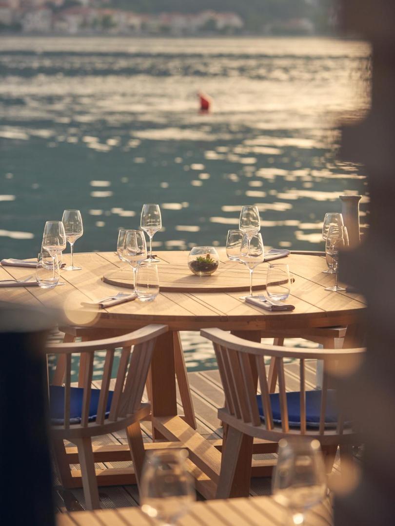 HUMA Kotor Bay Hotel & Villas restorāna terase ar klātu koka galdu un vīna glāzēm tieši pie Kotoras līča ūdens