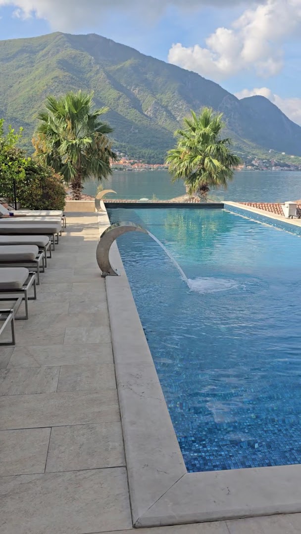 HUMA Kotor Bay Hotel & Villas garais āra baseins ar ūdens kaskādi, sauļošanās krēsliem un skatu uz kalniem