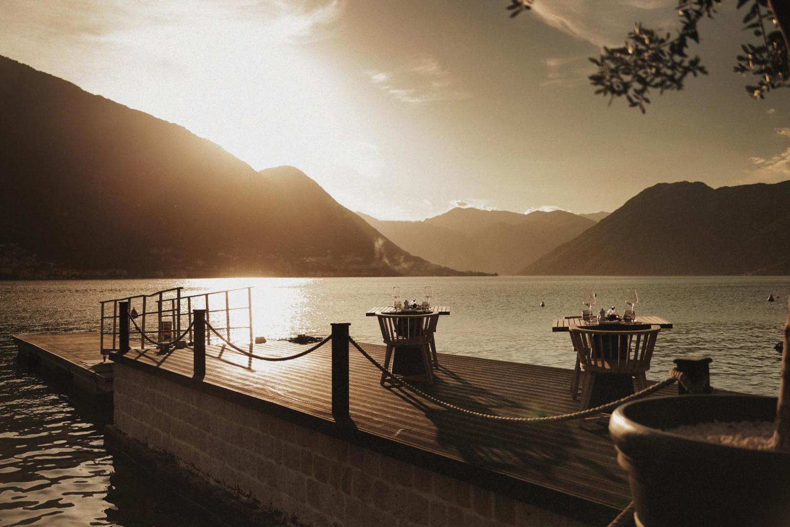 Romantiska galdiņa klājums uz koka laipas HUMA Kotor Bay Hotel & Villas kūrortā saulrieta laikā Melnkalnē