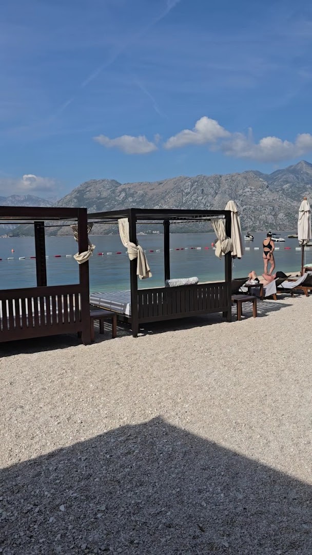 HUMA Kotor Bay Hotel & Villas pludmales atpūtas zona ar greznām bungalo tipa gultām un skatu uz kalniem Melnkalnē