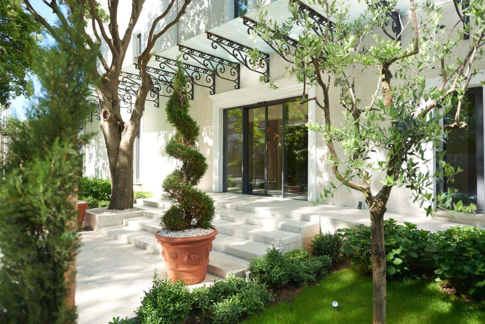HUMA Kotor Bay Hotel & Villas ieeja ar dekoratīviem augiem podos un modernu stikla nojumi pie galvenajām durvīm