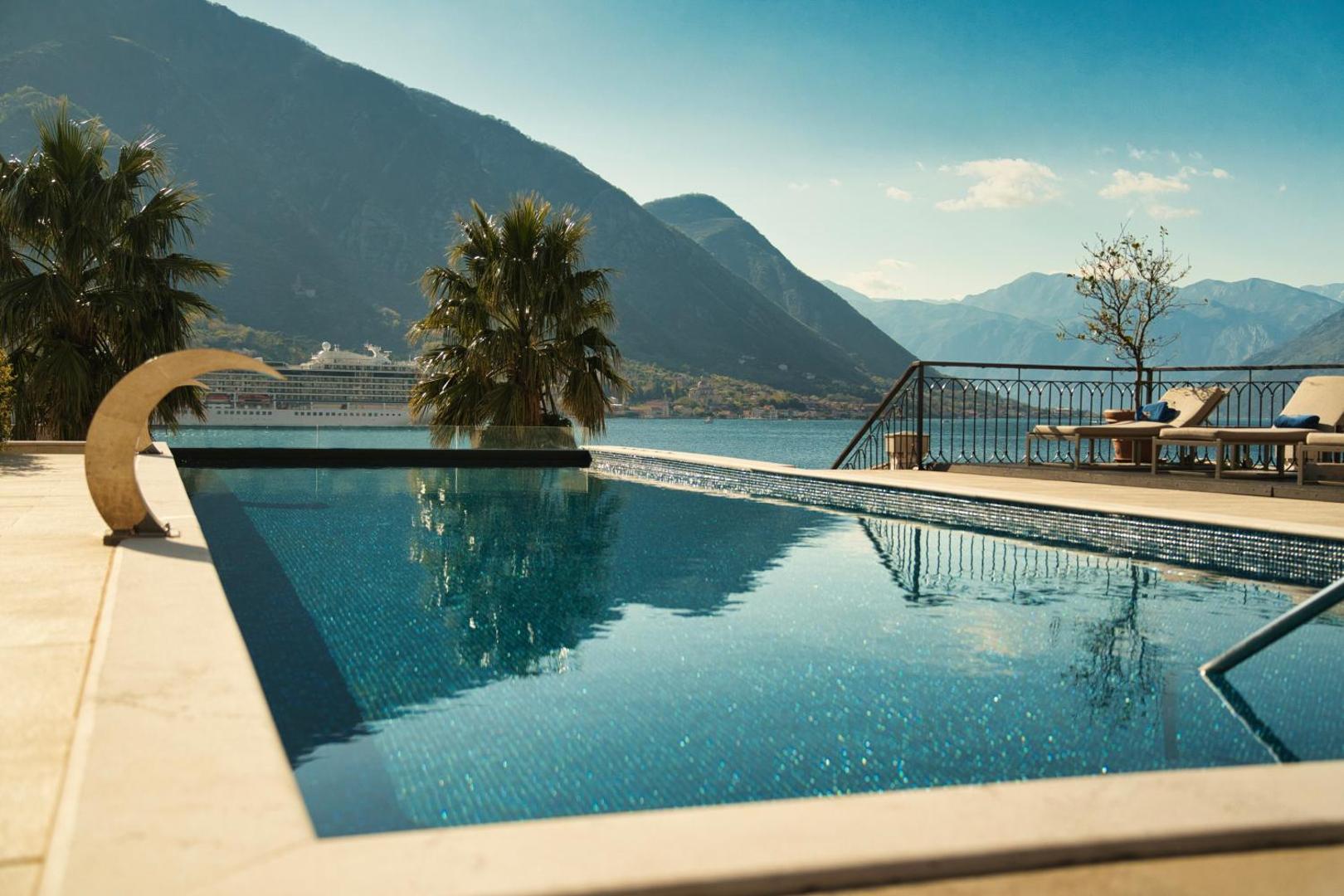 HUMA Kotor Bay Hotel & Villas āra baseins ar skatu uz Kotoras līci un kalniem, fonā redzams kruīza kuģis