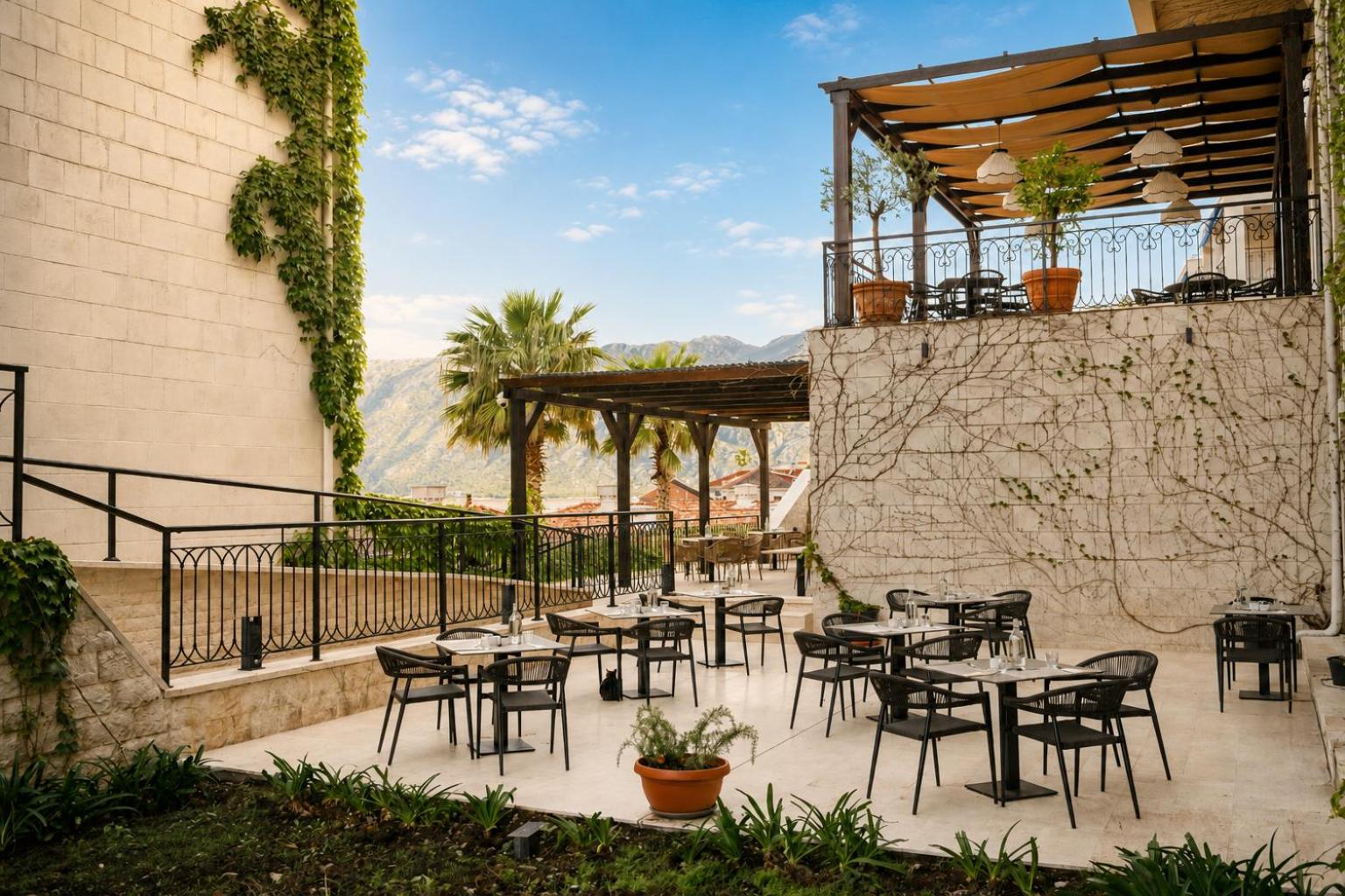 HUMA Kotor Bay Hotel & Villas akmens mūra iekšpagalms ar galdiņiem un zaļumiem pie viesnīcas fasādes