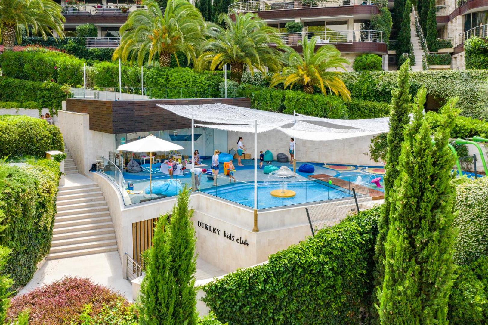 Dukley Kids Club āra zona ar bērnu baseinu un rotaļu laukumu, ko ieskauj zaļojoši dārzi un palmas