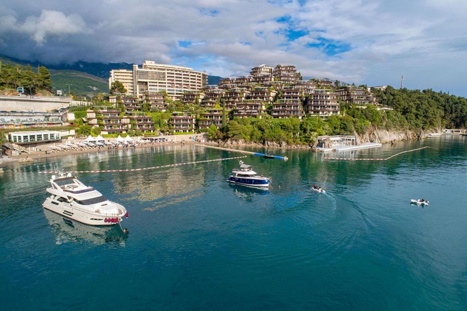 Dukley Hotel & Resort panorāmas skats no jūras puses Budvā, Melnkalnē — luksusa jahtas un viesnīcas komplekss piekrastes klintīs