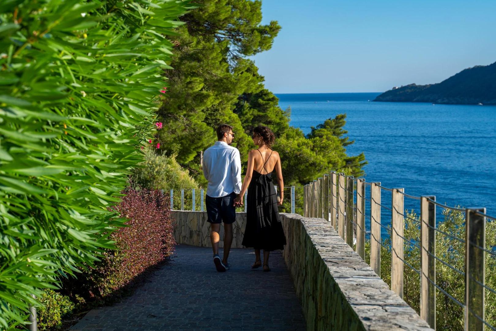 Pāris pastaigājas pa Dukley Hotel & Resort piekrastes promenādi ar skatu uz Adrijas jūru un zaļojošiem kalniem tālumā
