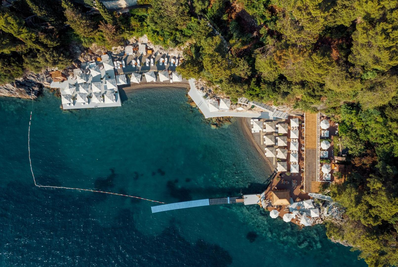 Dukley Hotel & Resort privātā līča skats no putna lidojuma — tirkīza ūdens, koku ieskauta pludmale ar baltiem saulessargiem un laipām