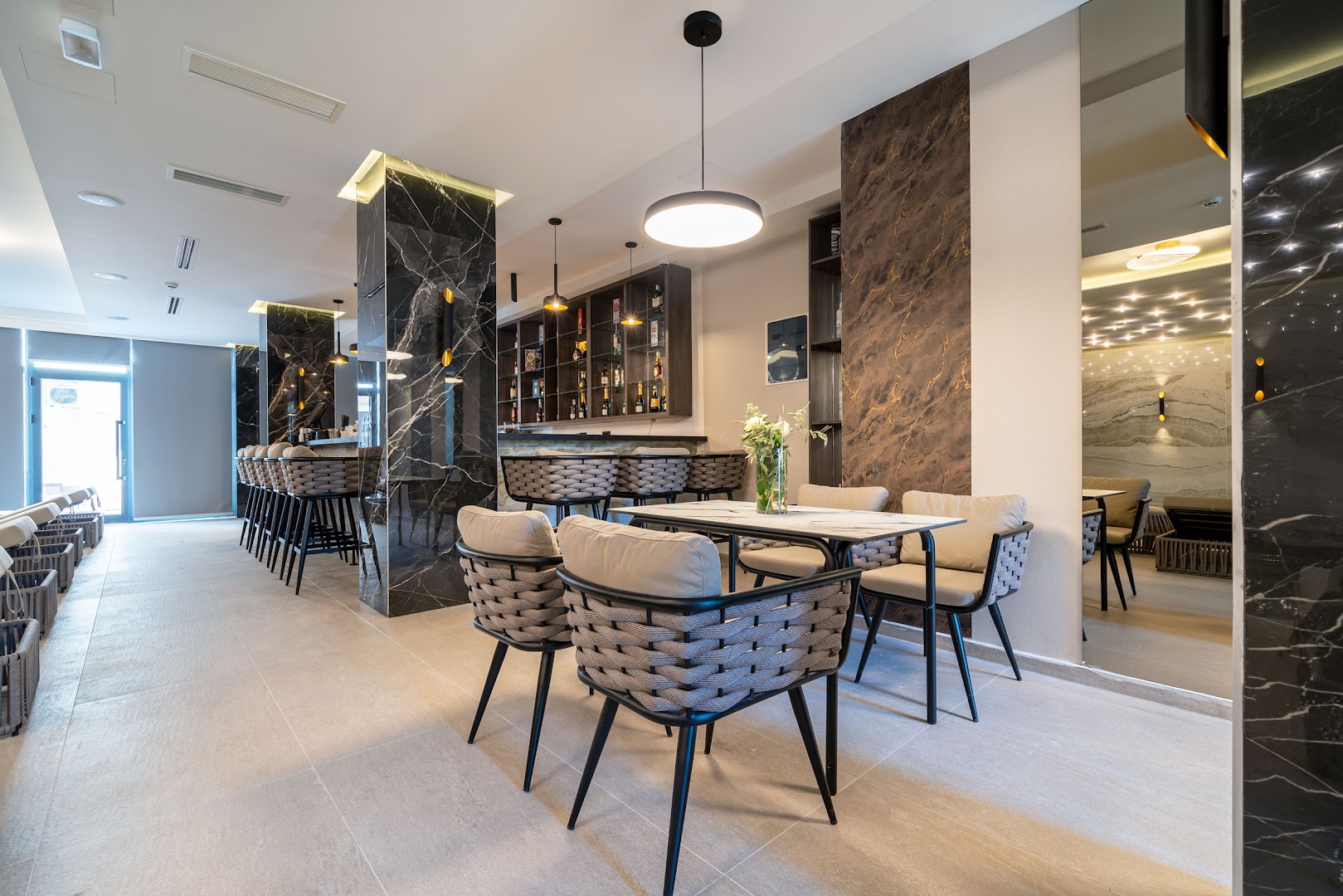 Hotel Millennium by Aycon bārs un restorāna zona ar modernām mēbelēm, tumša marmora kolonnām un izsmalcinātu apgaismojumu.