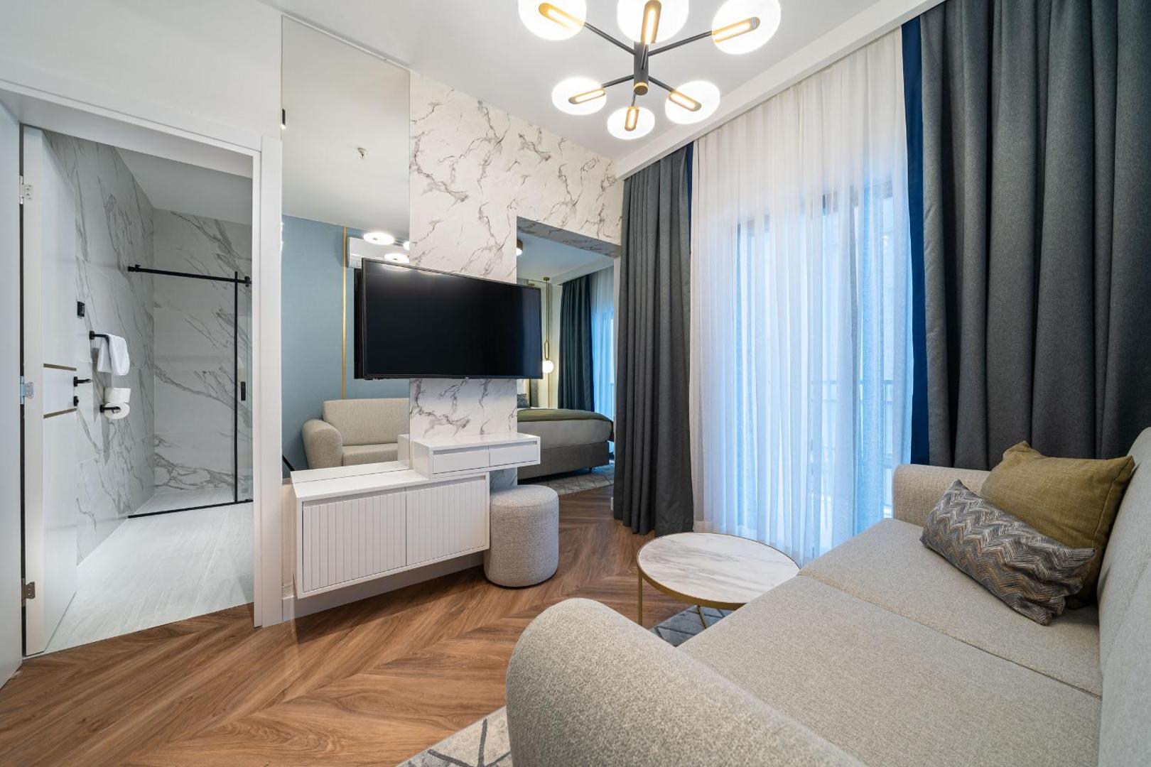 Hotel Millennium by Aycon numura dzīvojamā zona ar dīvānu, televizoru un ieeju modernā vannas numurā