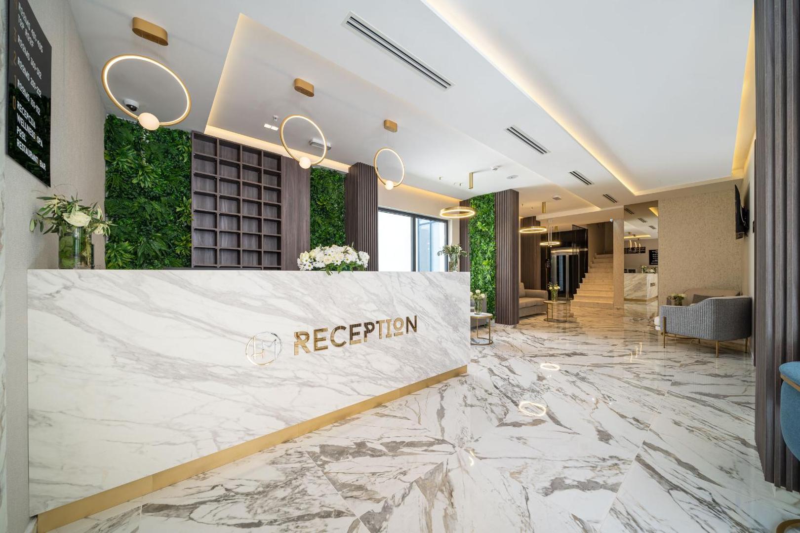 Moderna Hotel Millennium by Aycon recepcijas zona ar marmora apdari, zaļo augu sienu un zelta krāsas gaismas elementiem.