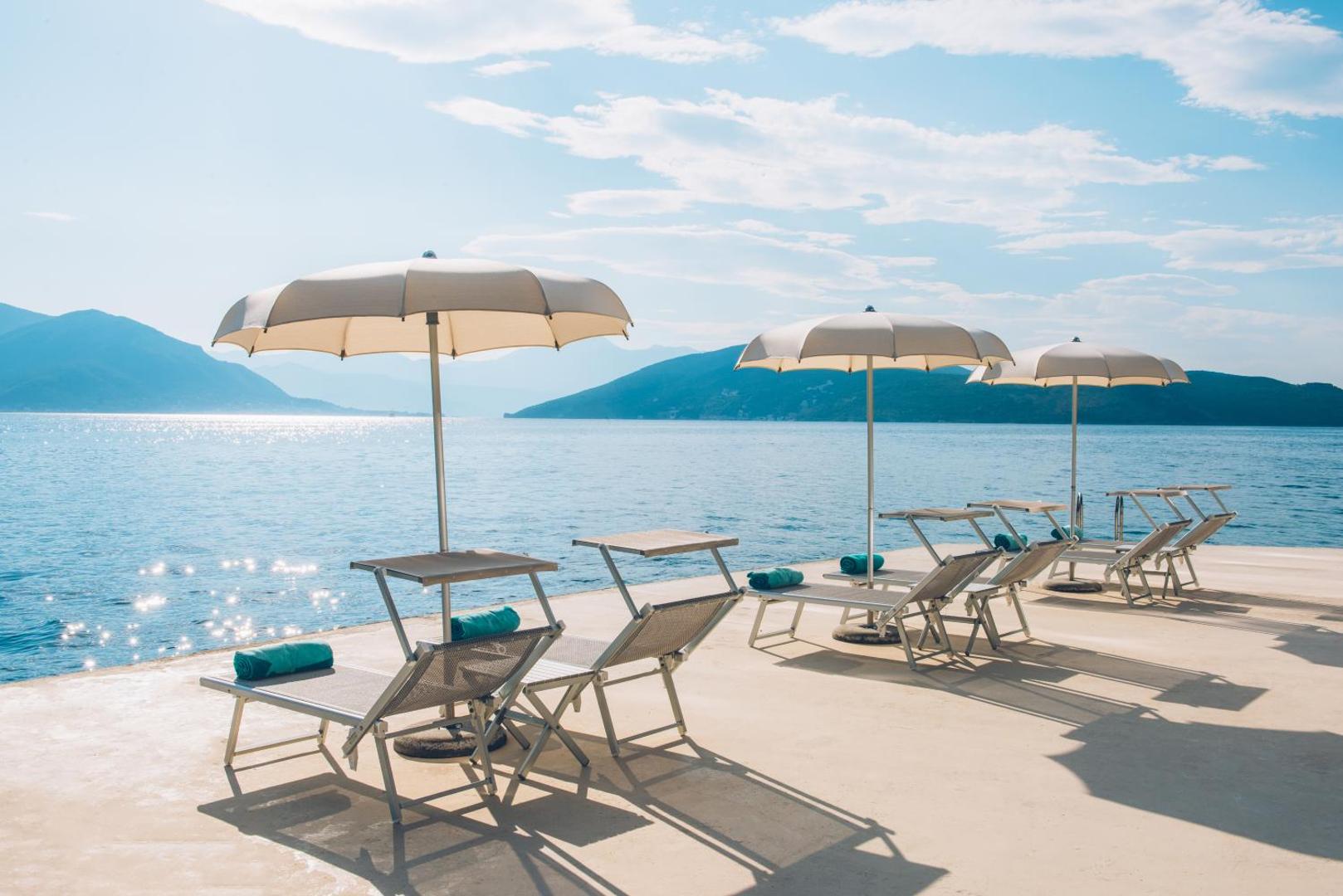 Iberostar Herceg Novi atpūtas zona ar sauļošanās krēsliem un saulessargiem uz terases ar skatu uz kalniem un līci
