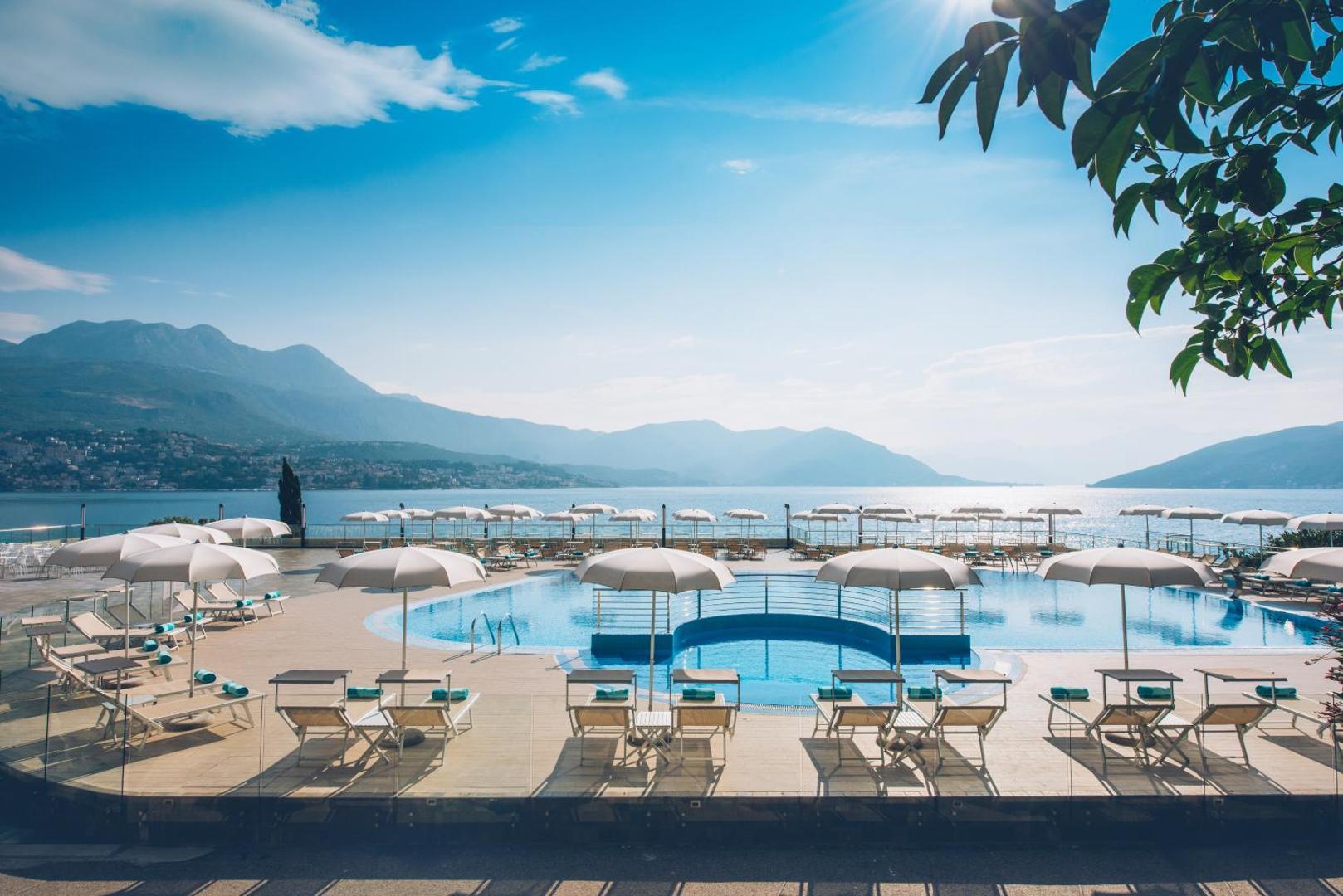 Iberostar Herceg Novi āra baseins ar saulessargiem un zviļņiem, fonā Kotoras līča ūdeņi un kalnu grēdas Melnkalnē