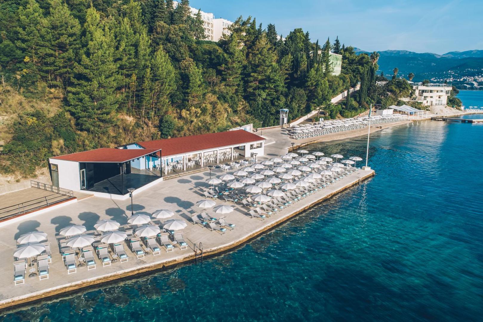Iberostar Herceg Novi viesnīcas teritorija no augšas — pludmales zona, restorāns un mežains kalns pie Adrijas jūras