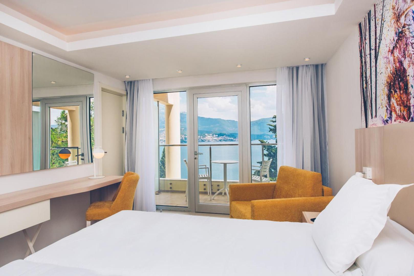 Iberostar Herceg Novi numura interjers ar darba zonu, dzeltenu atpūtas krēslu un skatu uz jūru caur stikla durvīm