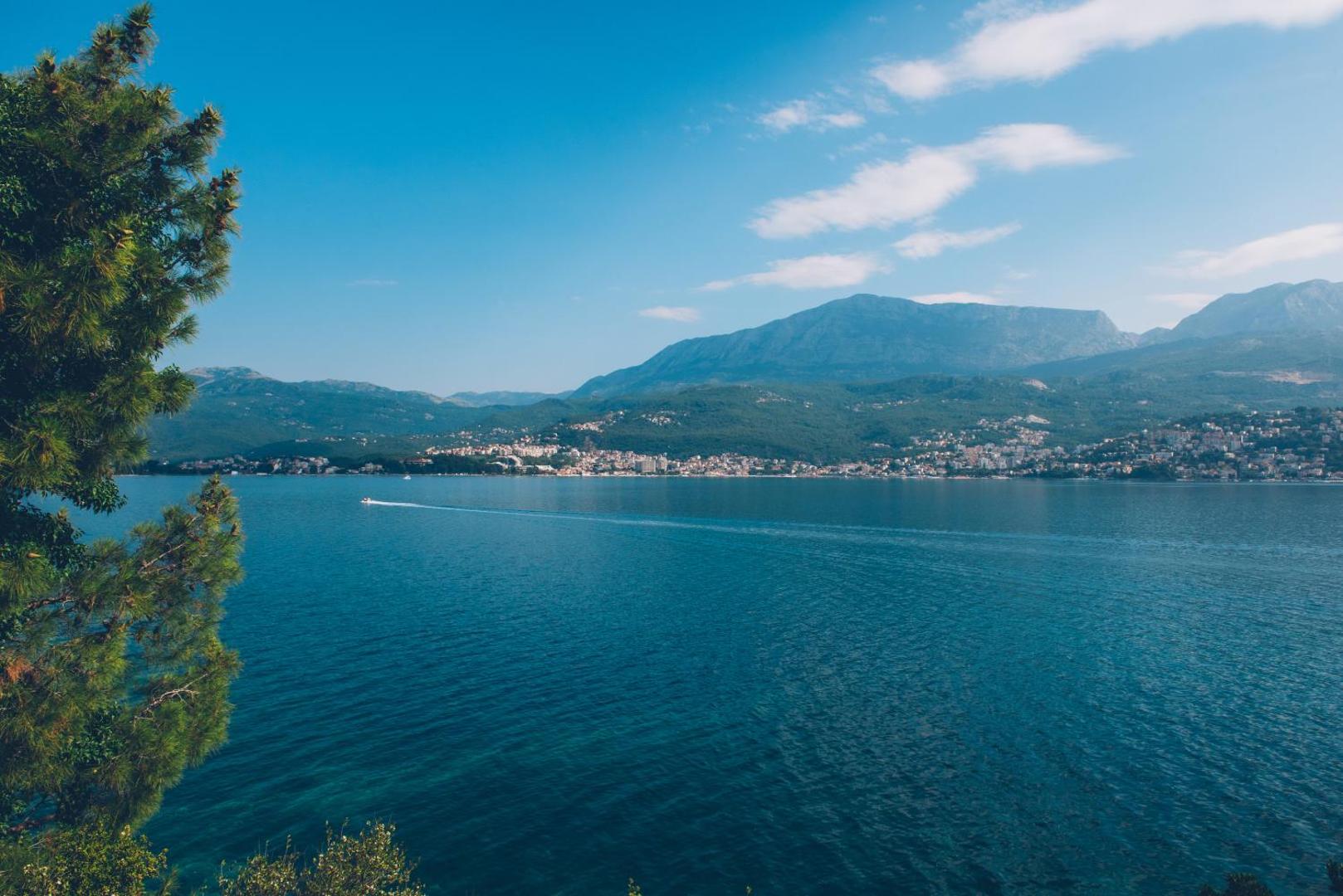Skats no Iberostar Herceg Novi uz Kotoras līča zilo ūdeni, kalniem un piekrastes pilsētu saulainā dienā