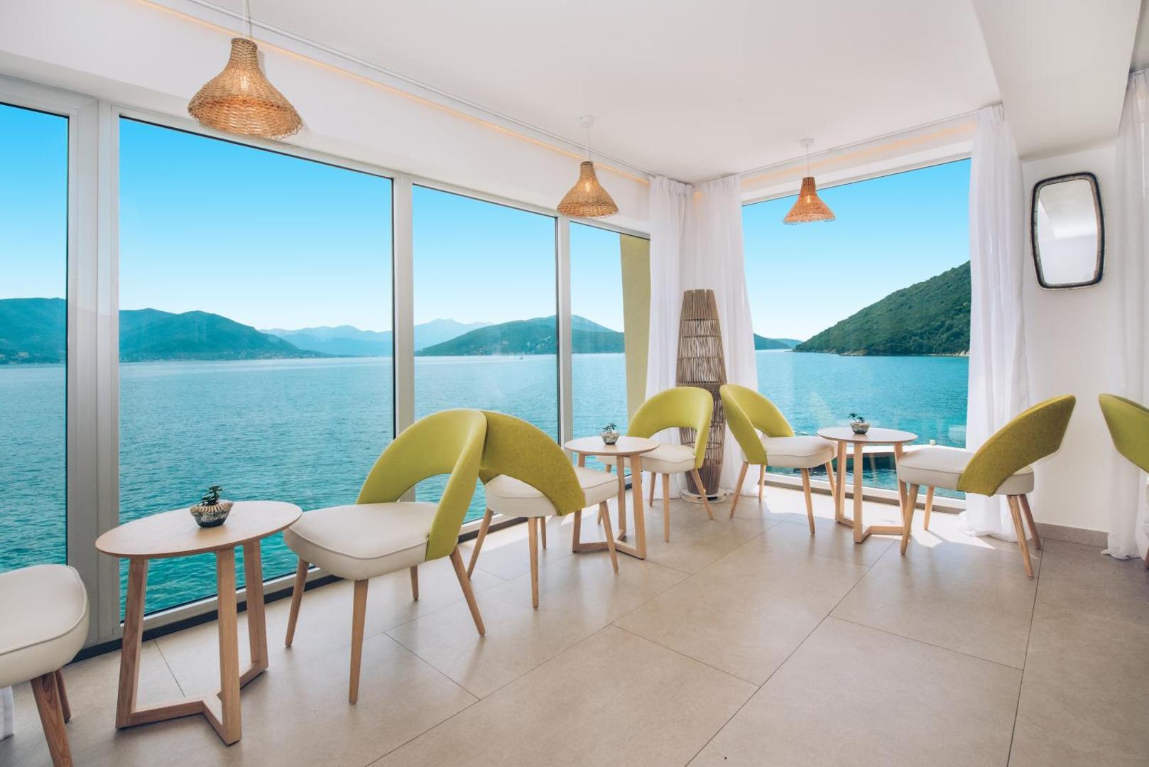 Iberostar Herceg Novi iekštelpu bārs ar moderniem krēsliem un panorāmas logiem, no kuriem paveras skats uz jūru un kalniem