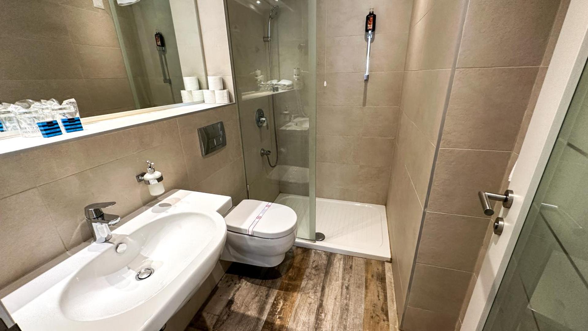 Gaiša Hotel Castellastva vannas istaba ar koka imitācijas grīdu, dušu un baltu izlietni viesnīcas numurā Melnkalnē