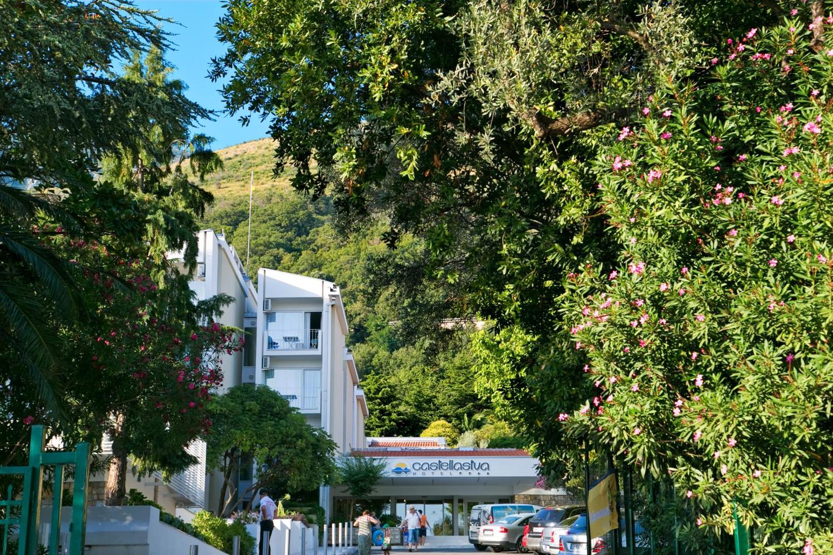 Skats uz Hotel Castellastva caur ziedošiem oleandriem un zaļiem kokiem Petrovacā, Melnkalnē