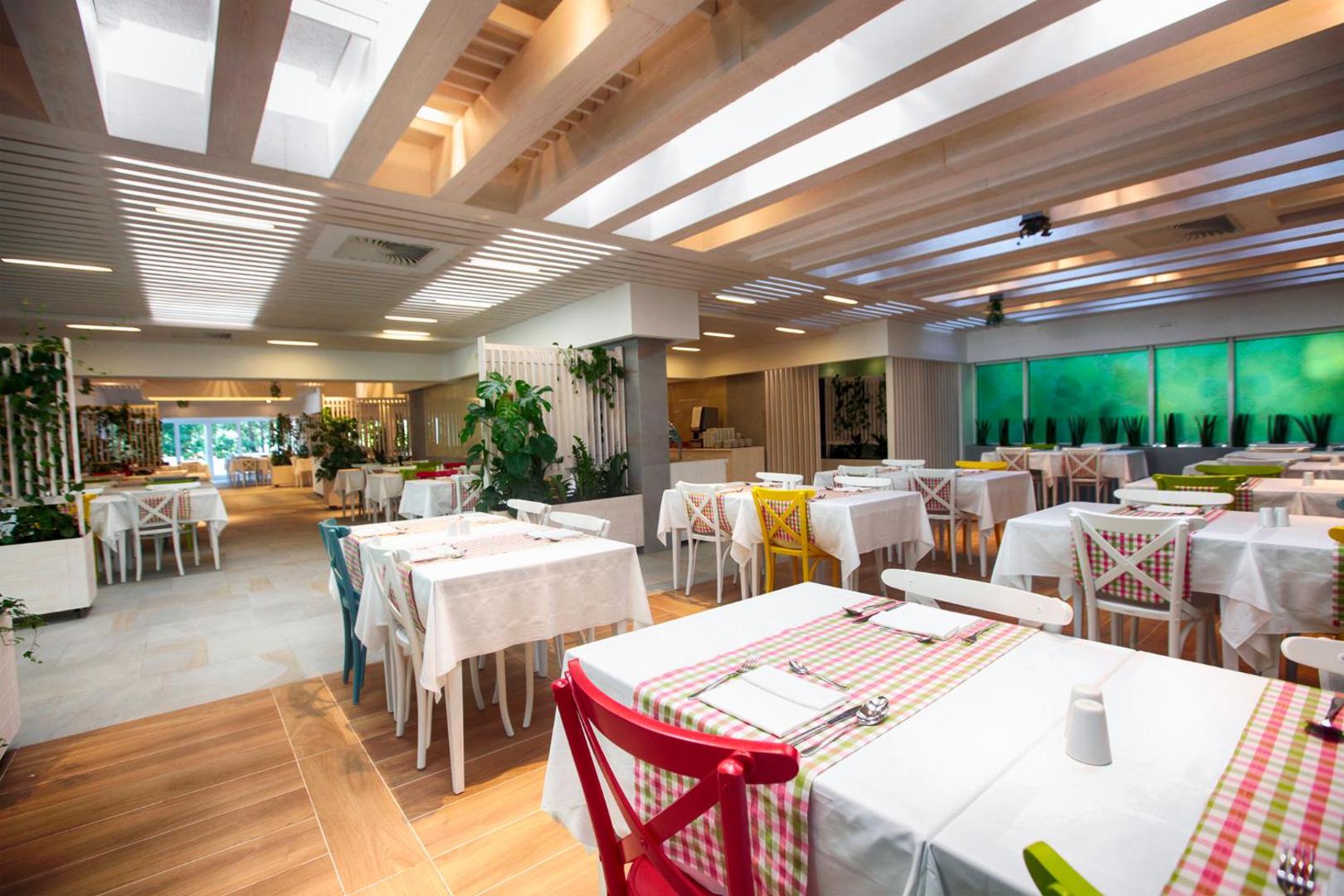 Hotel Castellastva galvenais restorāns Petrovacā ar gaišu interjeru, koka elementiem un krāsainiem krēsliem — plaša un mājīga ēdamzāle